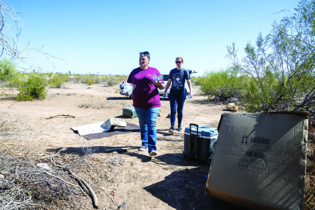 Manette and a volunteer carry waters as they walk towards a homeless encampment in the desert.