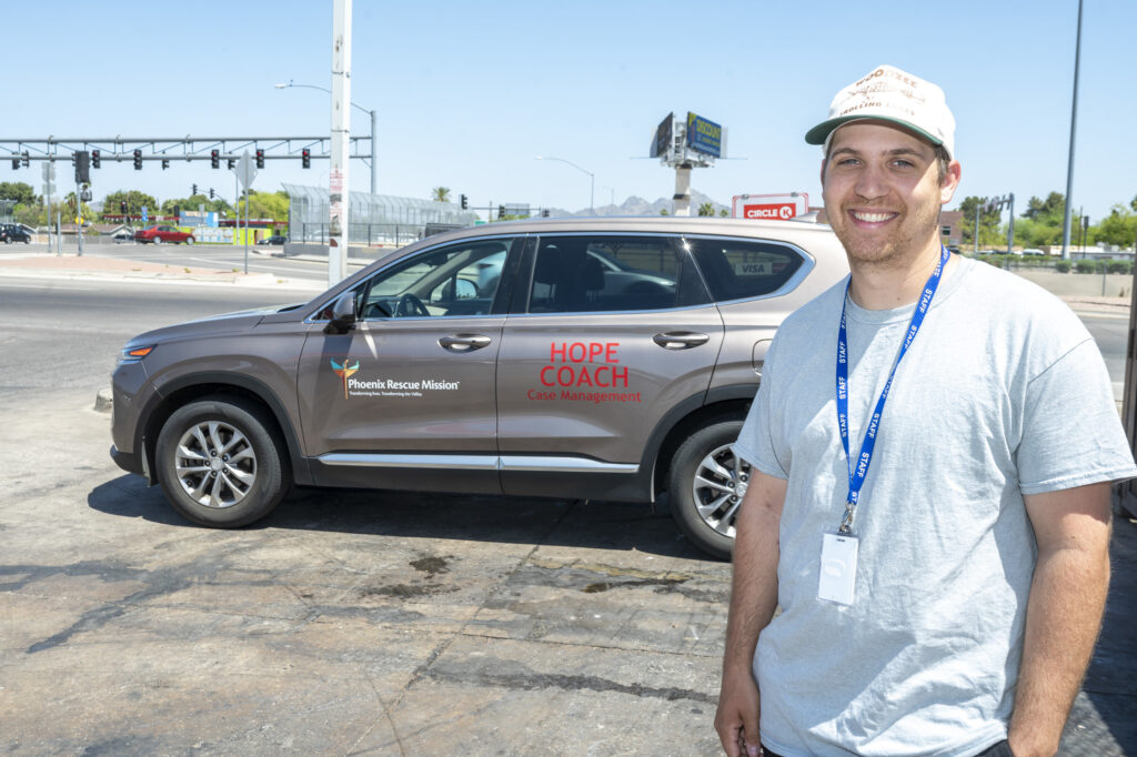 Steven looks at the camera in front of a Phoenix Rescue Mission Hope Coach vehicle by the side of the road.