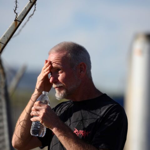 A man wipes his brow while facing the hot Phoenix sun, holding a bottle of water to his mouth.